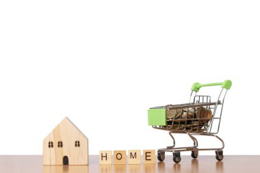 Alışveriş arabasında paralar, ahşap model bir ev ve beyaz arka planda izole edilmiş ahşap bloklardan yapılmış bir ev. kırpma yolu.