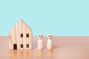 Ahşap bebek çifti mavi arka planda evin önünde duruyor. Aile evi, sigorta ve gayrimenkul yatırımı konsepti.