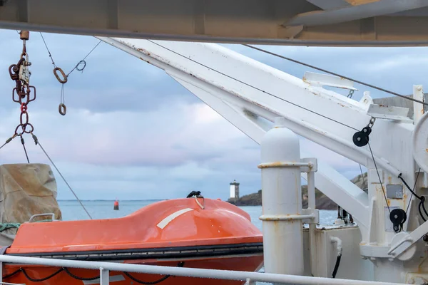 Transportation and safety at sea. Liferaft on ferry deck, orange lifeboat ready for evacuation from the board, hanging over a blue sea on the side of a cruise ship in the morning sun light