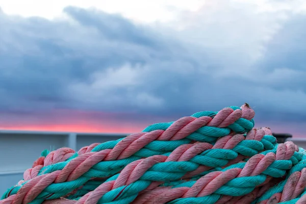 Nautical background. Colorful rope knot on the boat in beautiful moody light. Closeup of an old pink green frayed boat rope on sunrise with dramatic sky
