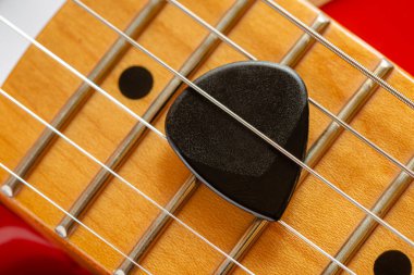Boynun ayrıntıları ve kırmızı elektro gitarın telleri, siyah bir plectrum ile aynı zamanda arabulucu olarak da bilinir.