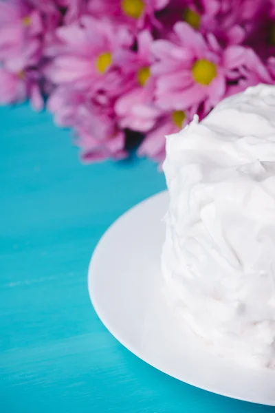 Biały tort kremowy z kwiatami na niebieskim tle drewniane — Zdjęcie stockowe