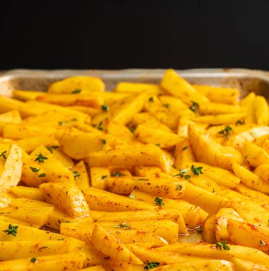 Tavada baharat ve bitkilerle dilimlenmiş çiğ patates pişirmeye hazır. Seçici odaklanma. Sığ alan derinliği.