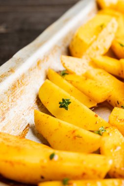 Tavada baharat ve bitkilerle dilimlenmiş çiğ patates pişirmeye hazır. Seçici odaklanma. Sığ alan derinliği.