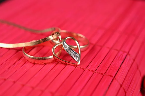 Dvě zlaté snubní prsteny a zlaté srdce — Stock fotografie