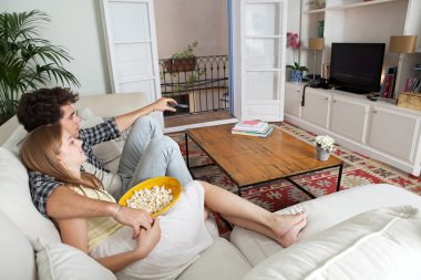 Couple watching television, eating pop corn