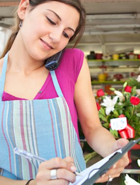 florist woman using the phone with a clipbard in her store
