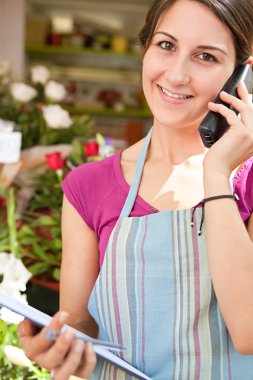 florist woman using the phone with a clipbard in her store