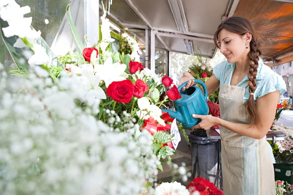 Цветочница поливает цветы и растения в своем магазине — стоковое фото