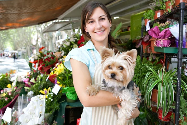 Florista mulher segurando um cão em sua loja — Fotografia de Stock