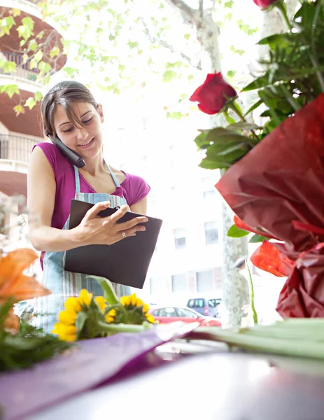 Florist woman using the phone with a clipbard in her store — ストック写真