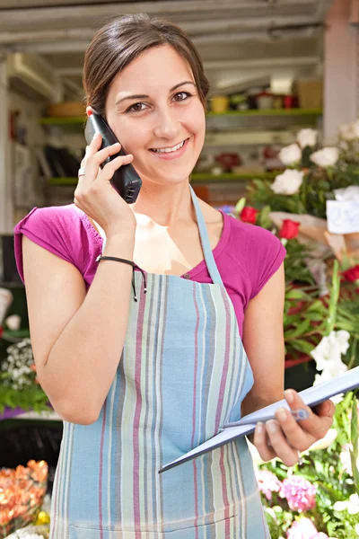 Florista mujer usando el teléfono con un portapapeles en su tienda — Foto de Stock