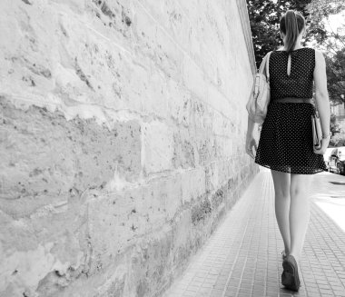 businesswoman walking along an old stone building wall