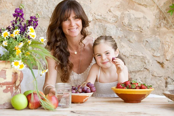 Mother and daughter eating fruits at table — Stockfoto