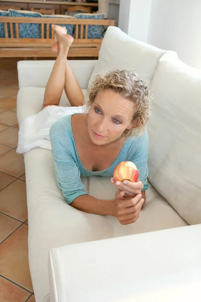 Donna che mangia una mela su un divano a casa — Foto Stock