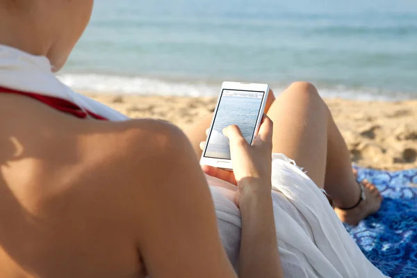 Donna su una spiaggia in riva al mare utilizzando uno smartphone — Foto Stock