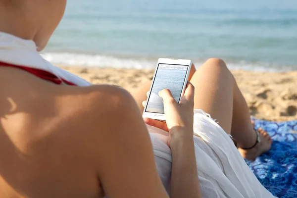 Woman on a beach by the sea using a smartphone — 스톡 사진