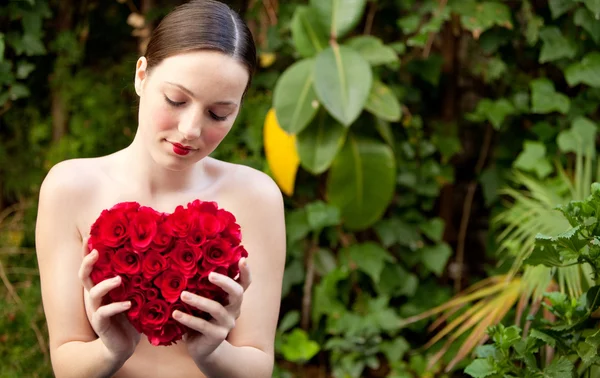 Nude girl holding a red roses heart in a garden — Stok fotoğraf