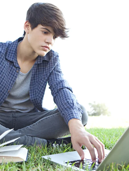 Junge liest ein Buch und benutzt einen Laptop — Stockfoto