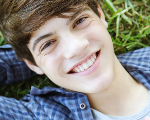 Student boy laying down on green grass in a park — Stock fotografie