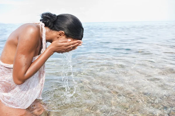 Black woman splashing sea water on her face — Stockfoto