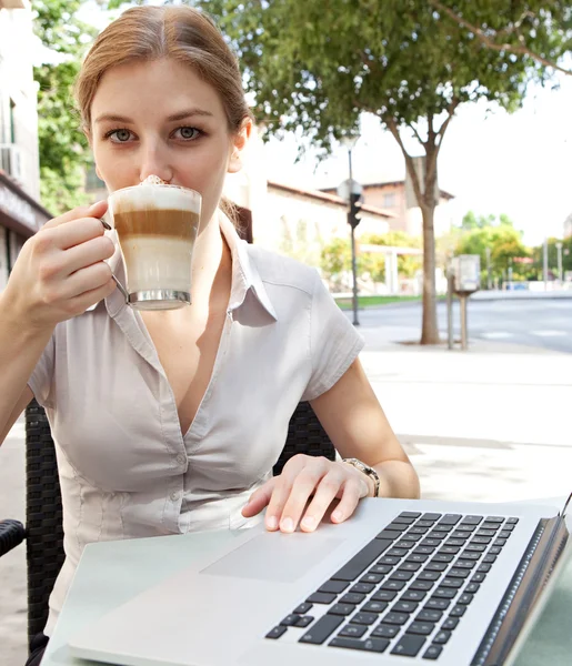 Donna d'affari che beve un caffè caldo della bevanda e usando un computer portatile — Foto Stock