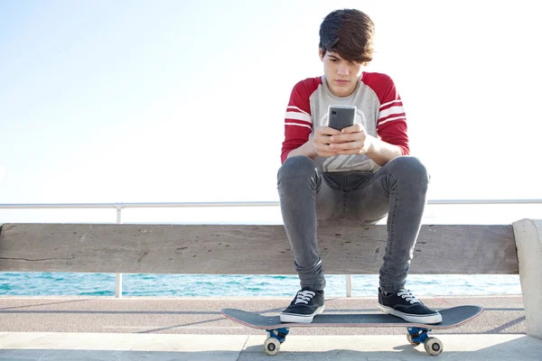 Boy with a skateboard using a smartphone — Stockfoto