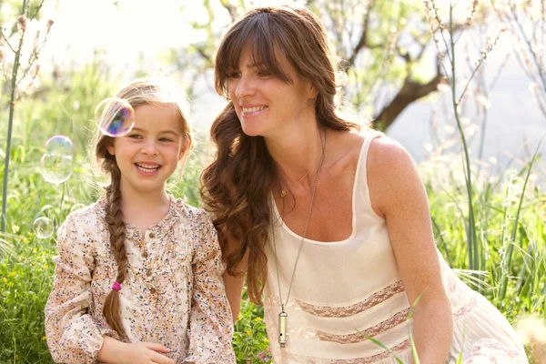 Mother and daughter playing to blow floating bubbles — Stock Photo, Image