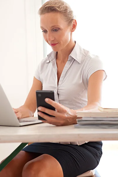 Mujer usando un dispositivo de teléfono inteligente y una computadora portátil — Foto de Stock