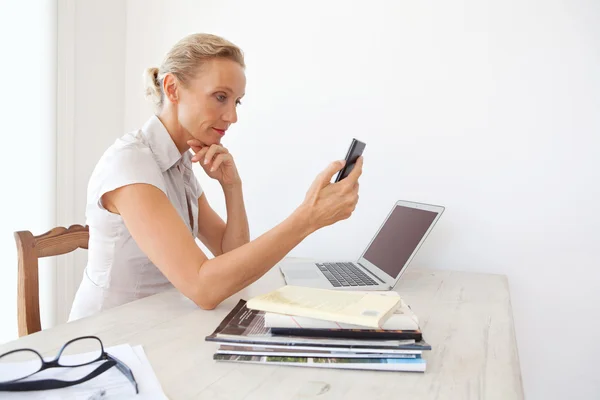 Mujer usando un dispositivo de teléfono inteligente y una computadora portátil — Foto de Stock