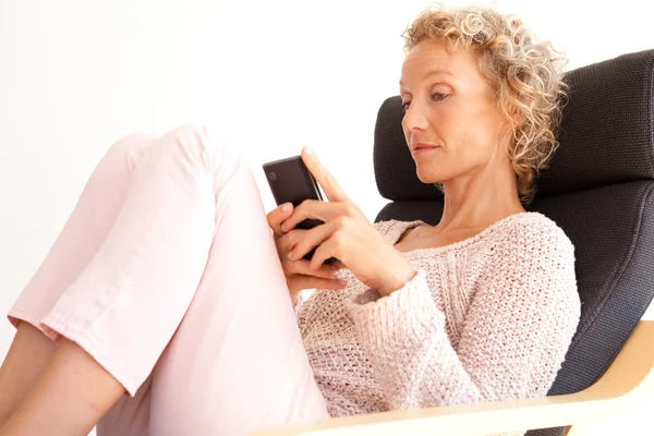 Woman in an armchair using a smartphone — Stockfoto