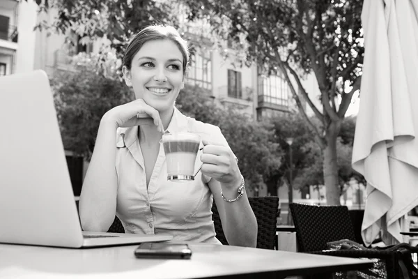 Businesswoman drinking a beverage and using laptop — Stockfoto