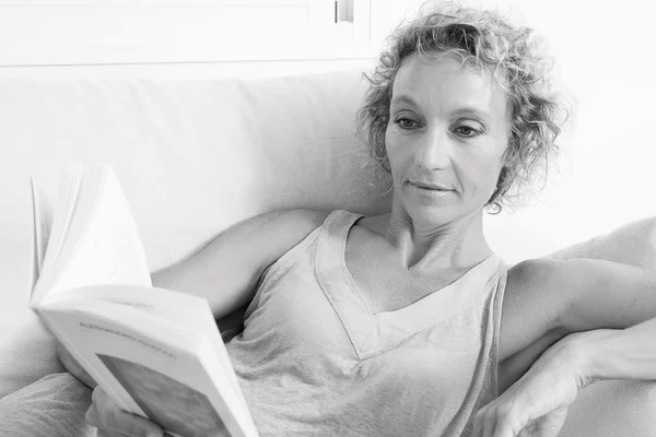 Woman reading book on a sofa at home — Stockfoto