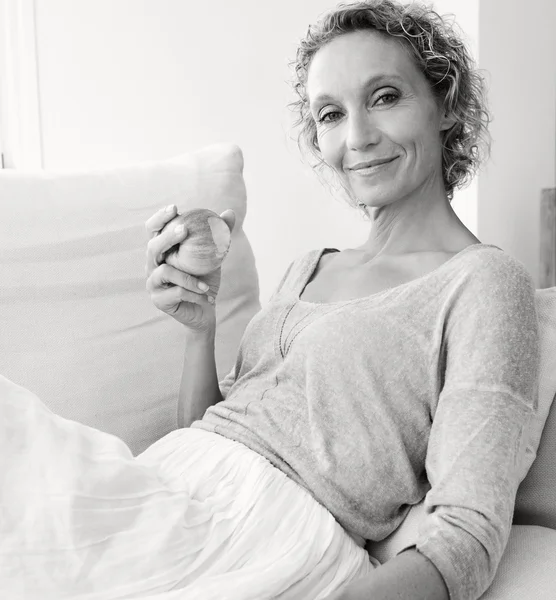 Mulher comendo uma maçã em um sofá em casa — Fotografia de Stock