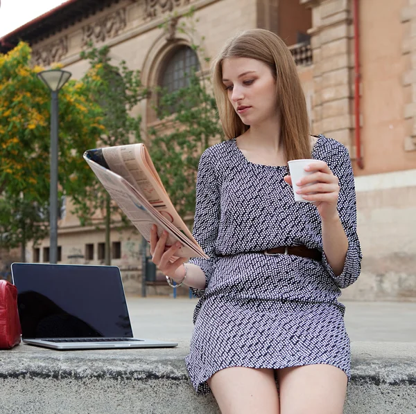 Business woman reading a financial newspaper while drinking coffee — Stok fotoğraf