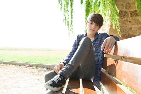 Boy sitting on a wooden bench in a park — Stok fotoğraf