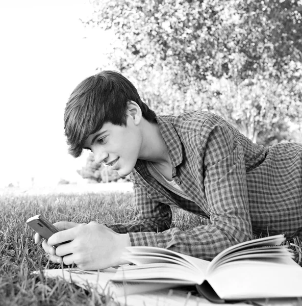 Boy with books and using a smartphone in the park — Stockfoto