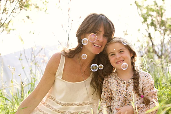 Мати і дочка грають, щоб підірвати плавучі бульбашки — стокове фото