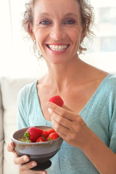 Woman eating a strawberries on a couch at home — Stockfoto