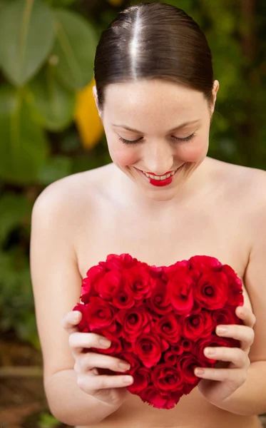 Nude girl holding a red roses heart in a garden — Stok fotoğraf