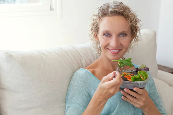 woman eating a salad on a couch at home
