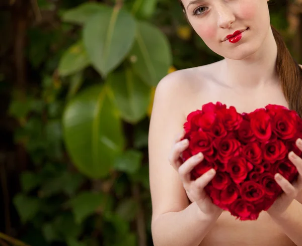 Nude girl holding a red roses heart in a garden — Stockfoto