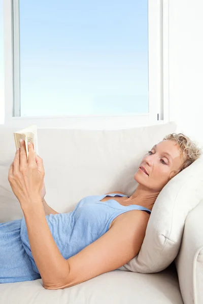 Woman reading book on a sofa at home — 图库照片