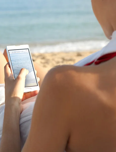Mujer en una playa junto al mar usando un smartphone — Foto de Stock