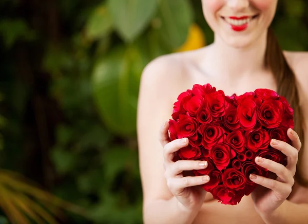 Nude girl holding a red roses heart in a garden — Stok fotoğraf