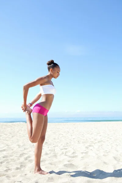 Woman stretching her legs, exercising and training on a beach — 图库照片