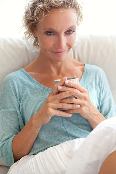 Woman drinking tea on a sofa at home — ストック写真