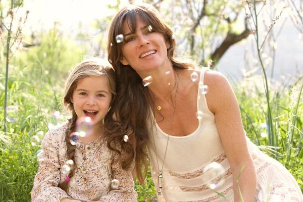 Mother and daughter playing to blow floating bubbles — Stock Photo, Image