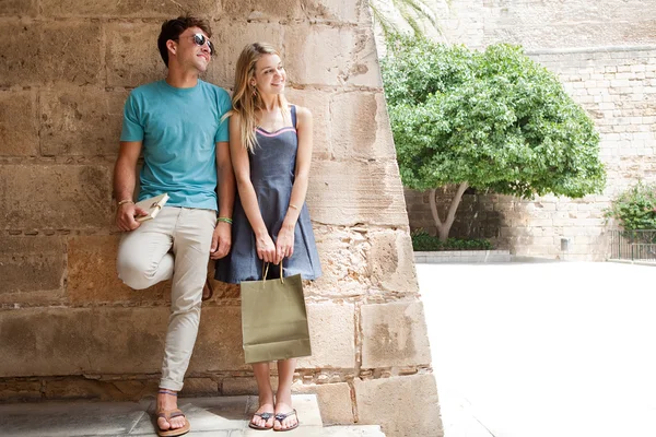 Couple smiling against an wall and carrying shopping bags — Stock Photo, Image