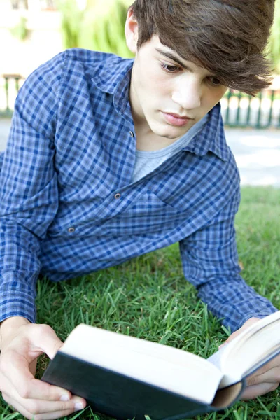 Adolescente menino lendo um livro de texto na grama — Fotografia de Stock